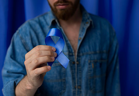 Hombre sosteniendo en su mano una cinta azul por el día del cáncer de próstata