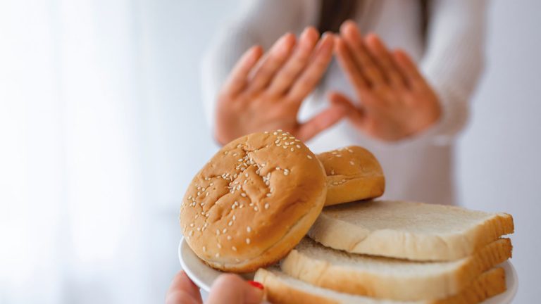 mujer rechazando con las manos un plato de pan - Enfermedad Celíaca