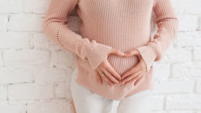 Mujer marcando un corazón con sus manos en una barriga de un reciente embarazo - Prueba de embarazo